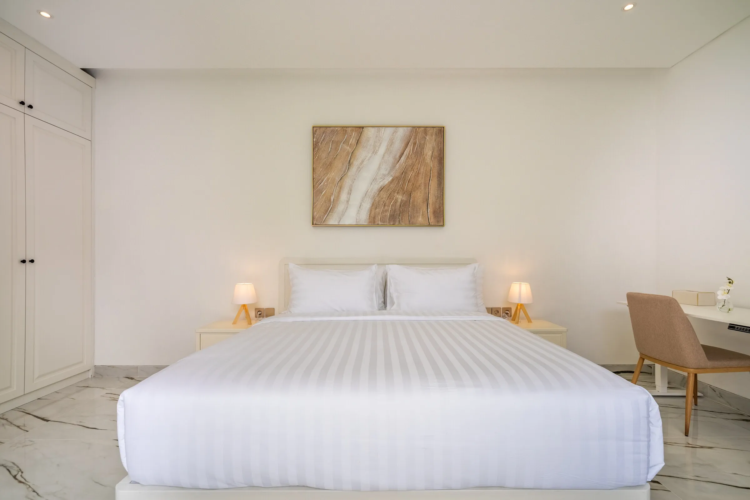 Bedroom with white linen, bedside lamps and timber desk chair