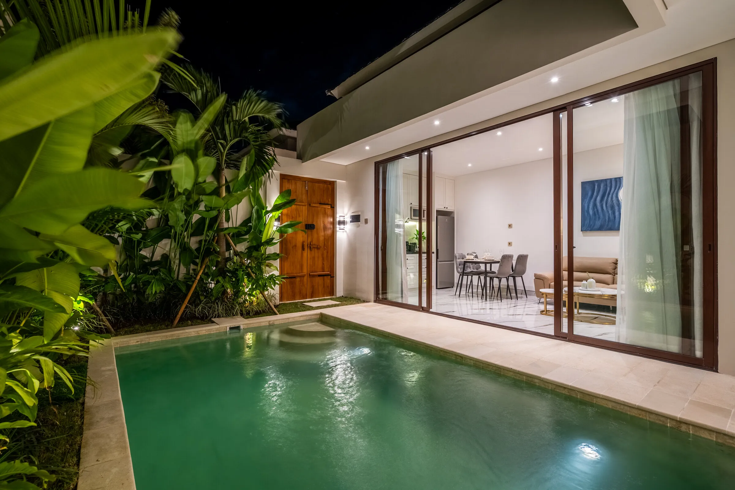 The villa pool lit at night with garden uplighting